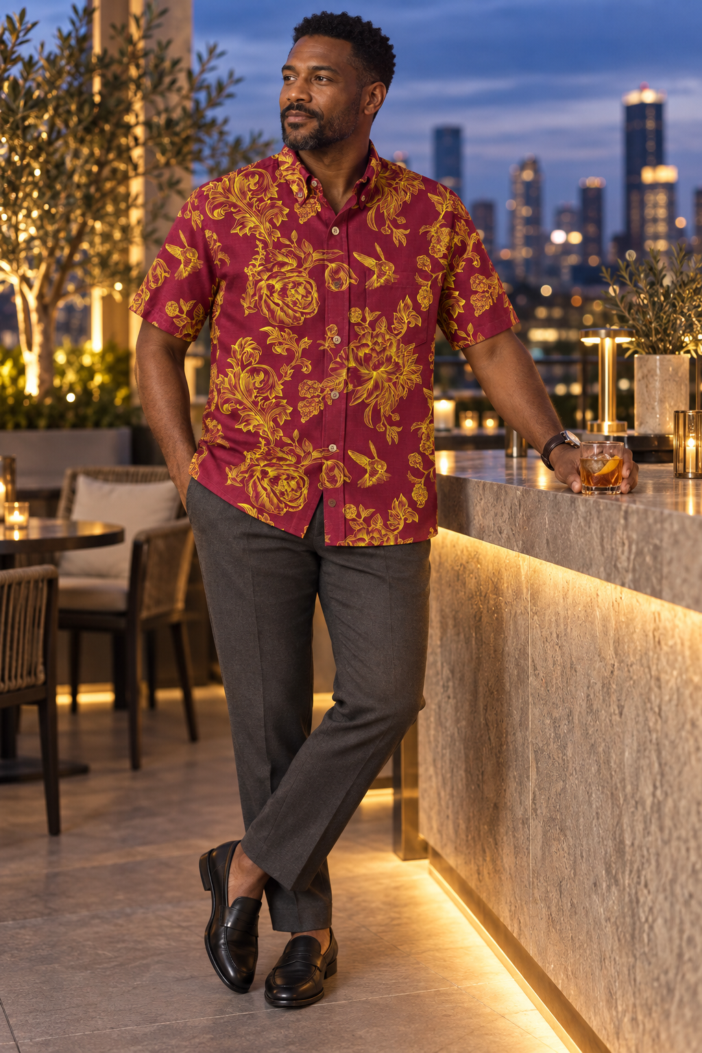 Man wearing the Engraved Hummingbird Garden Resort Shirt in Crimson Gold at a rooftop bar